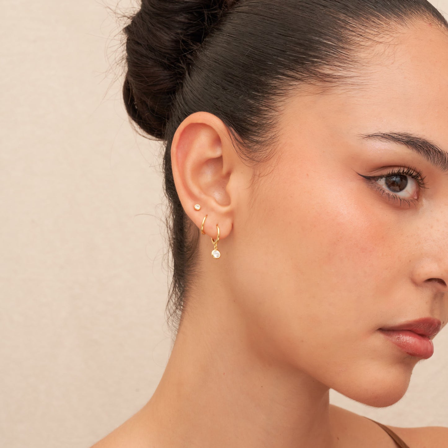 Close-up of a woman wearing gold hoop earrings with a beige background