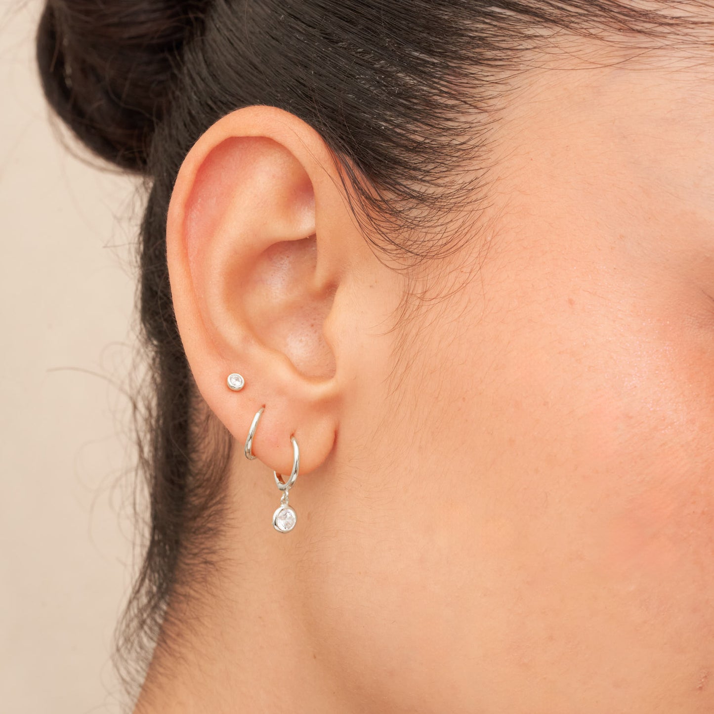 Close-up of an ear wearing two silver hoop earrings on a beige background