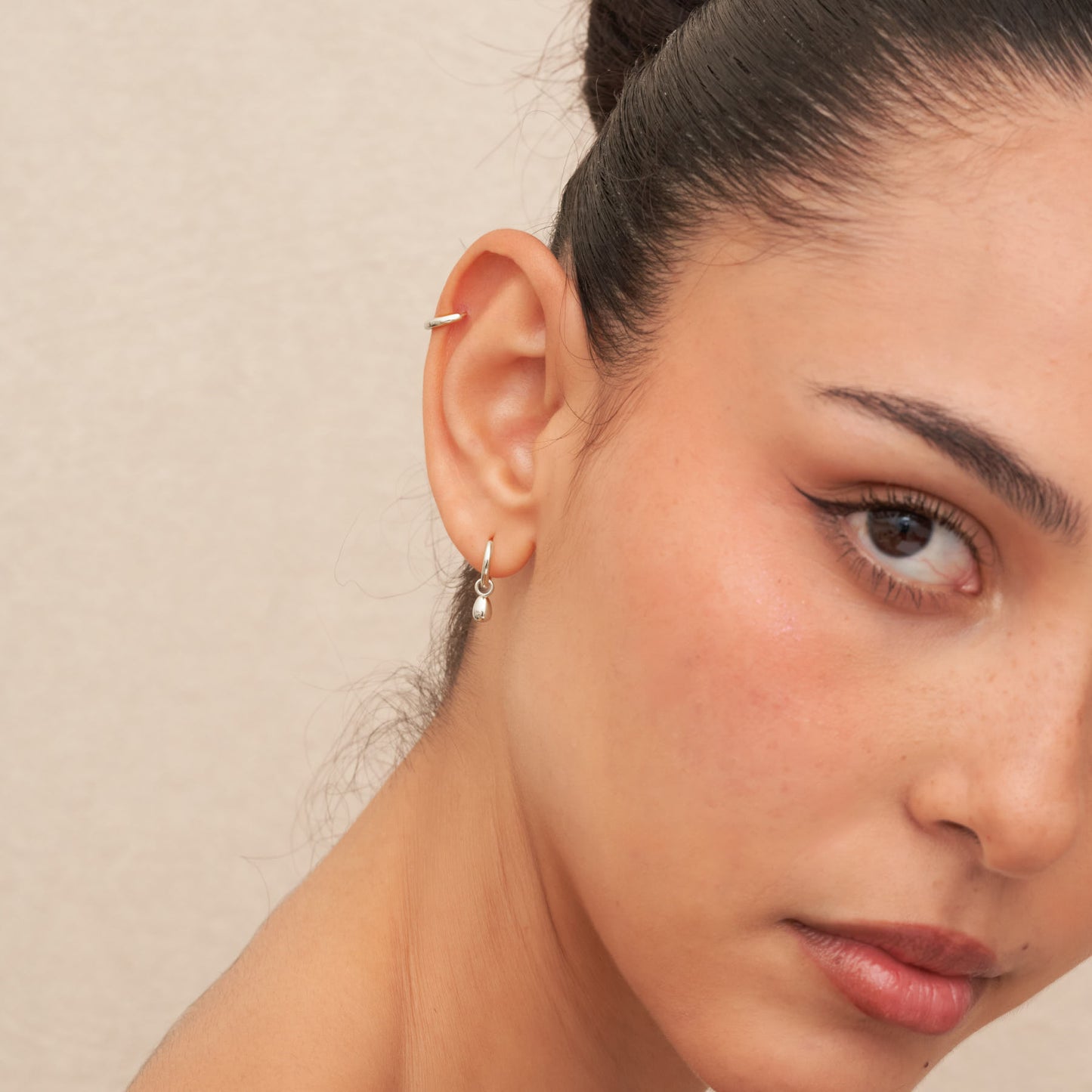 Close-up of a woman wearing a silver hoop earring against a neutral background