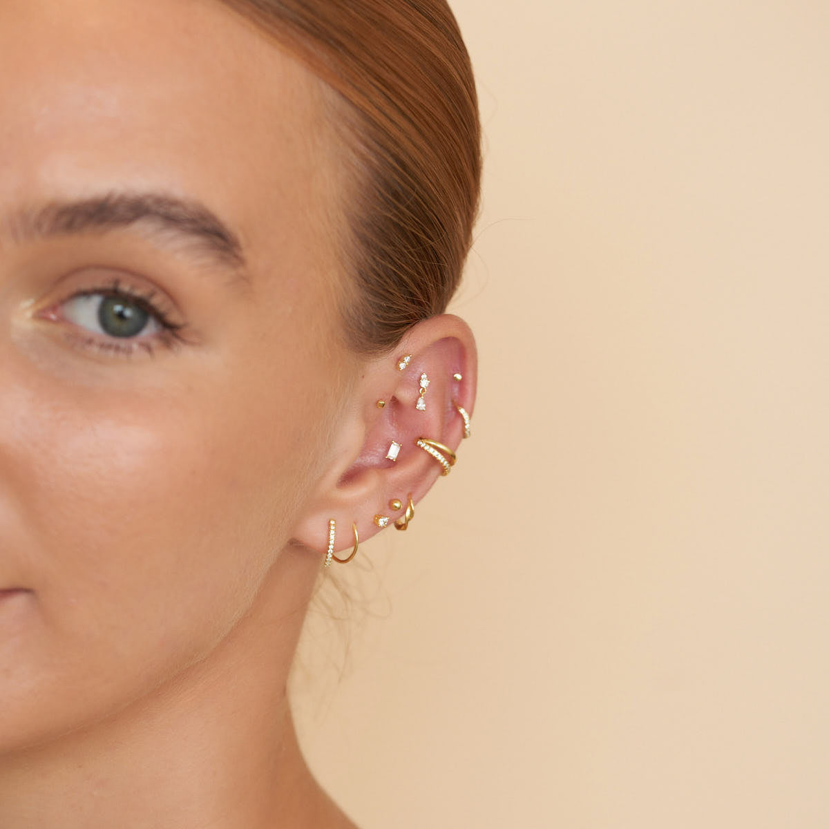 Close-up of a person wearing gold hoop earrings on a beige background