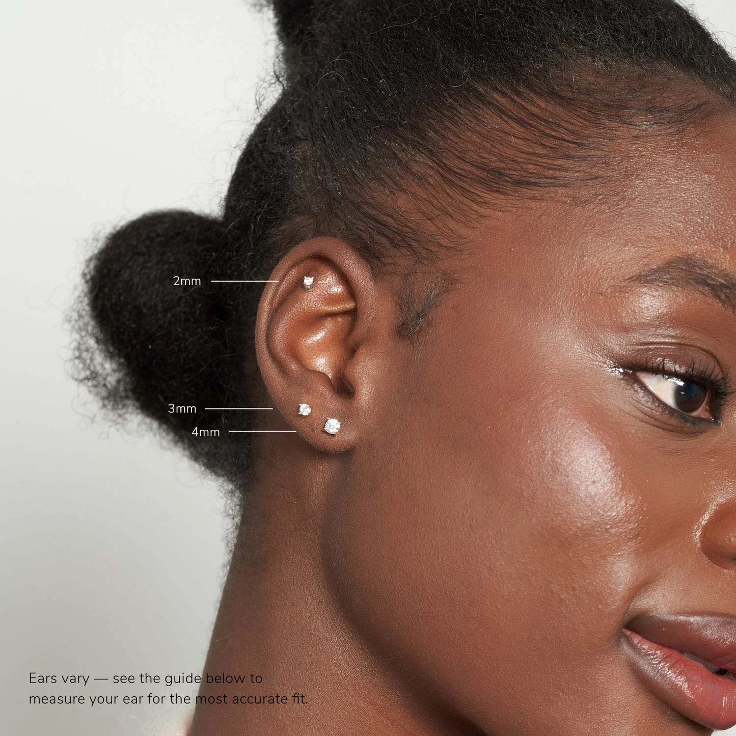 Close-up of an ear with earrings, showing measurement points, on a plain background.