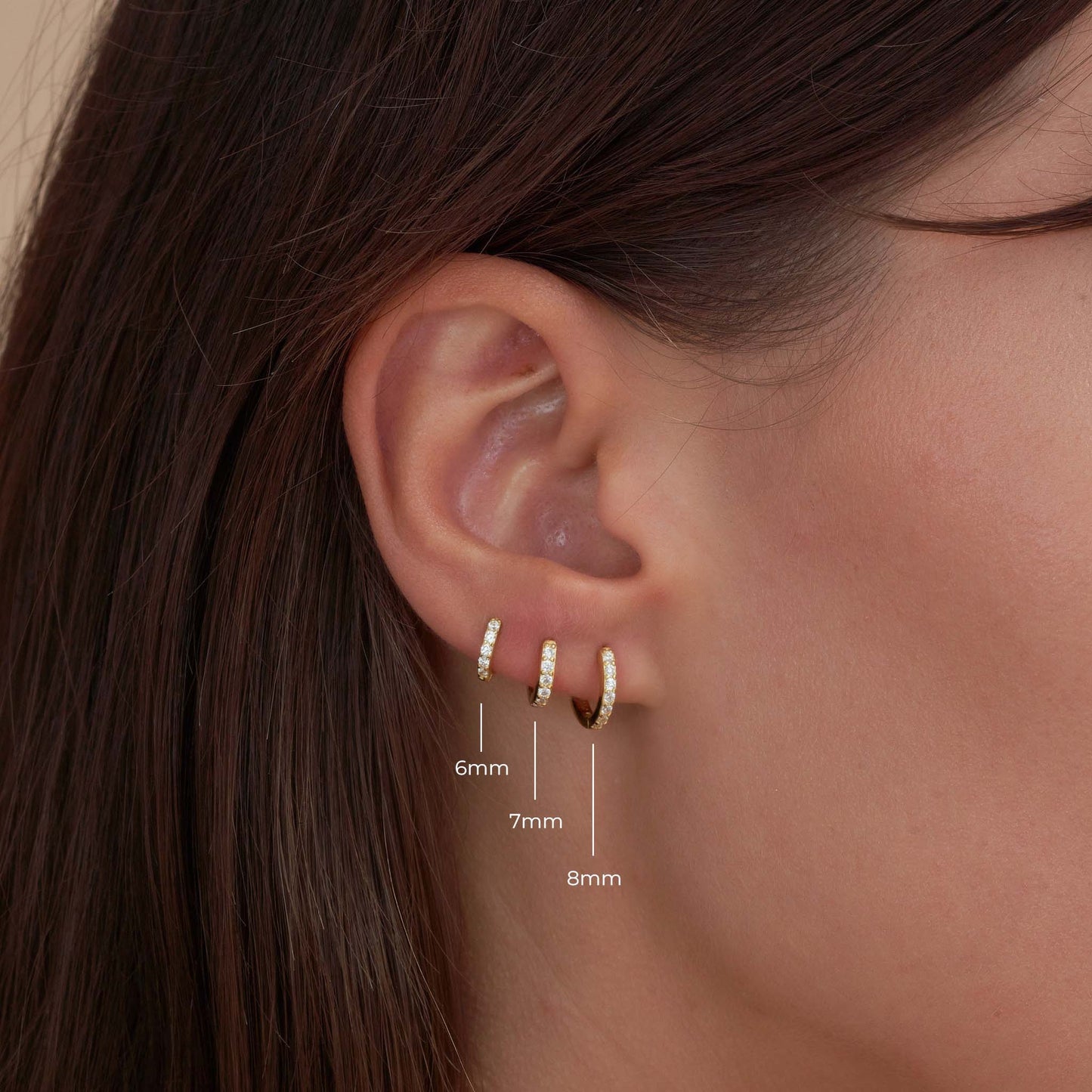 Close-up of an ear wearing gold hoop earrings with size measurements.