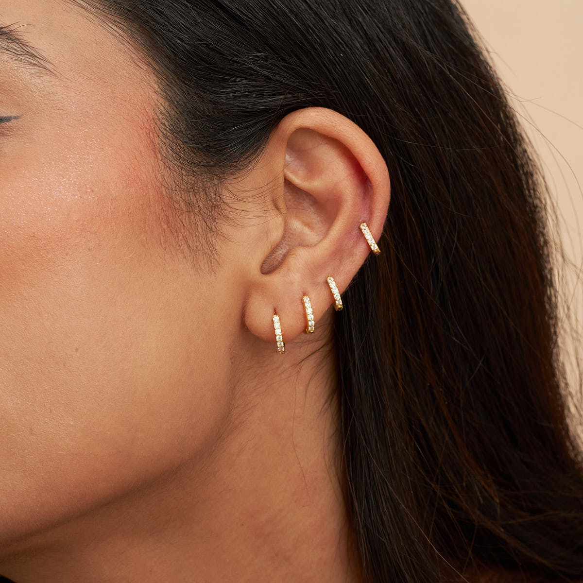 Close-up of an ear with multiple gold hoop earrings on a neutral background