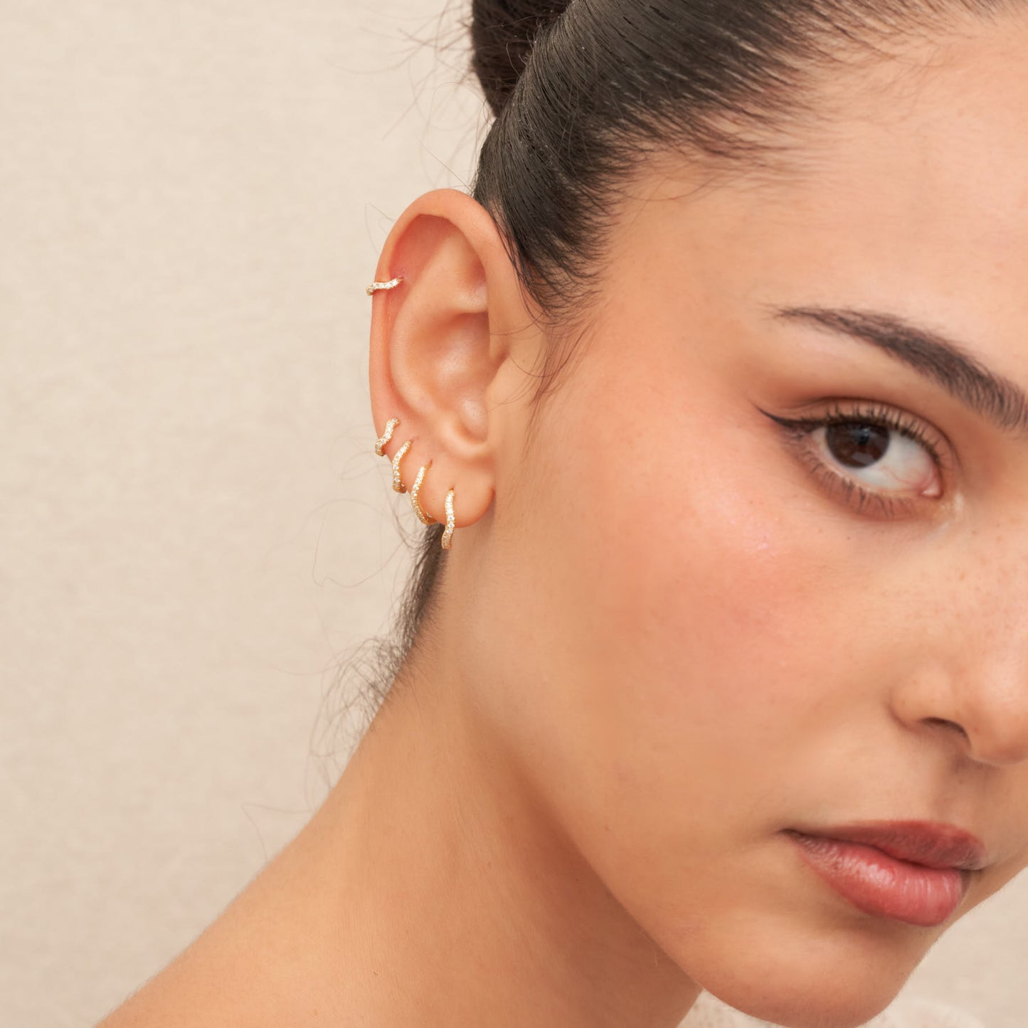 Close-up of a woman's ear with gold earrings against a neutral background