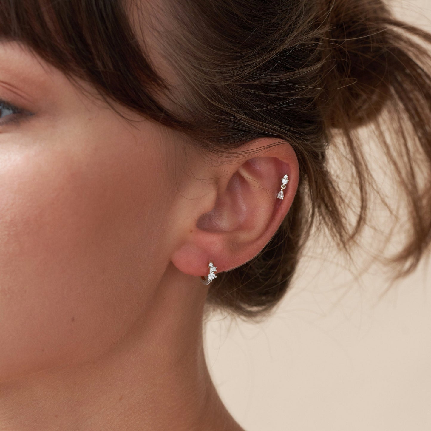 Close-up of a woman's ear wearing diamond stud earrings with a neutral background