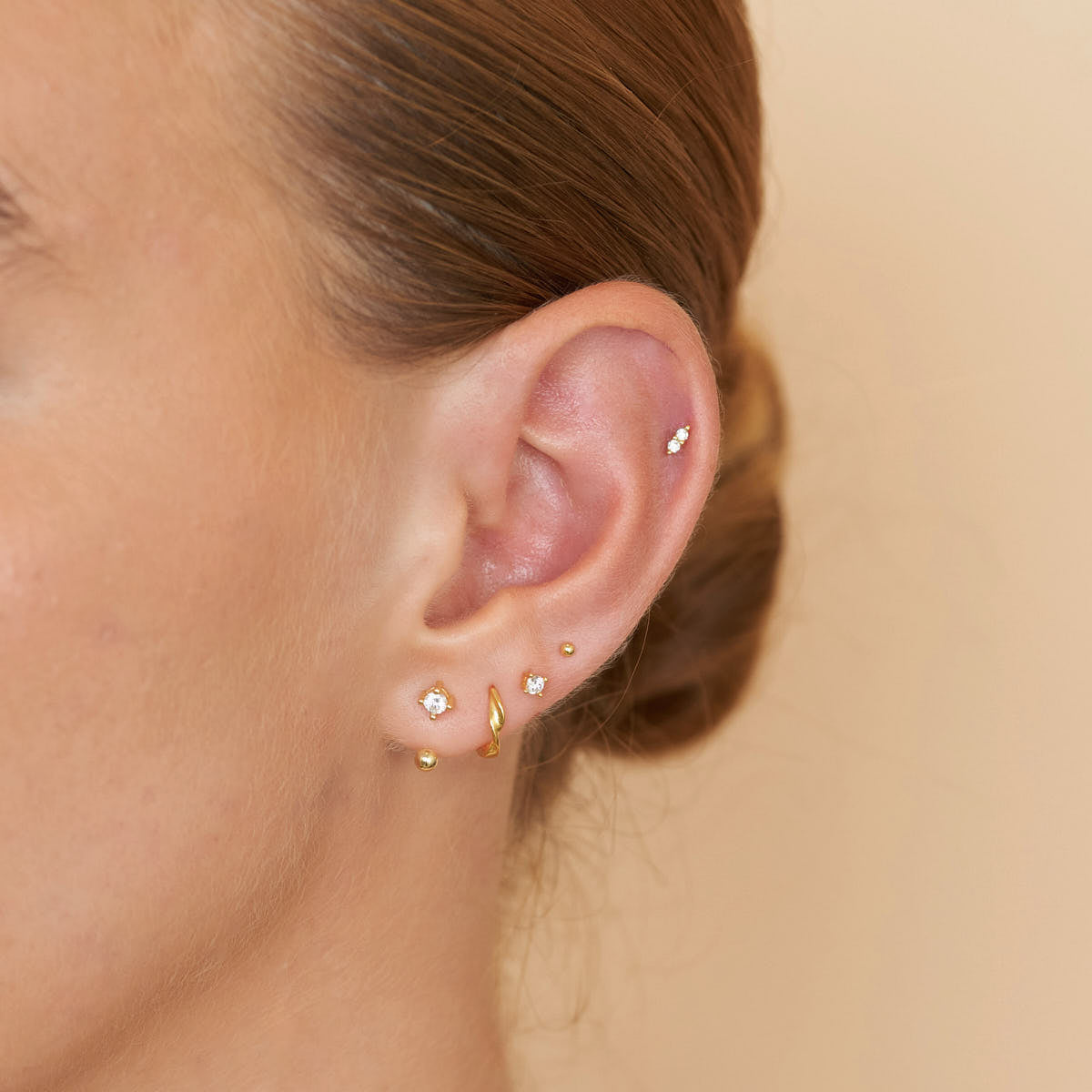 Close-up of an ear with multiple gold earrings on a beige background
