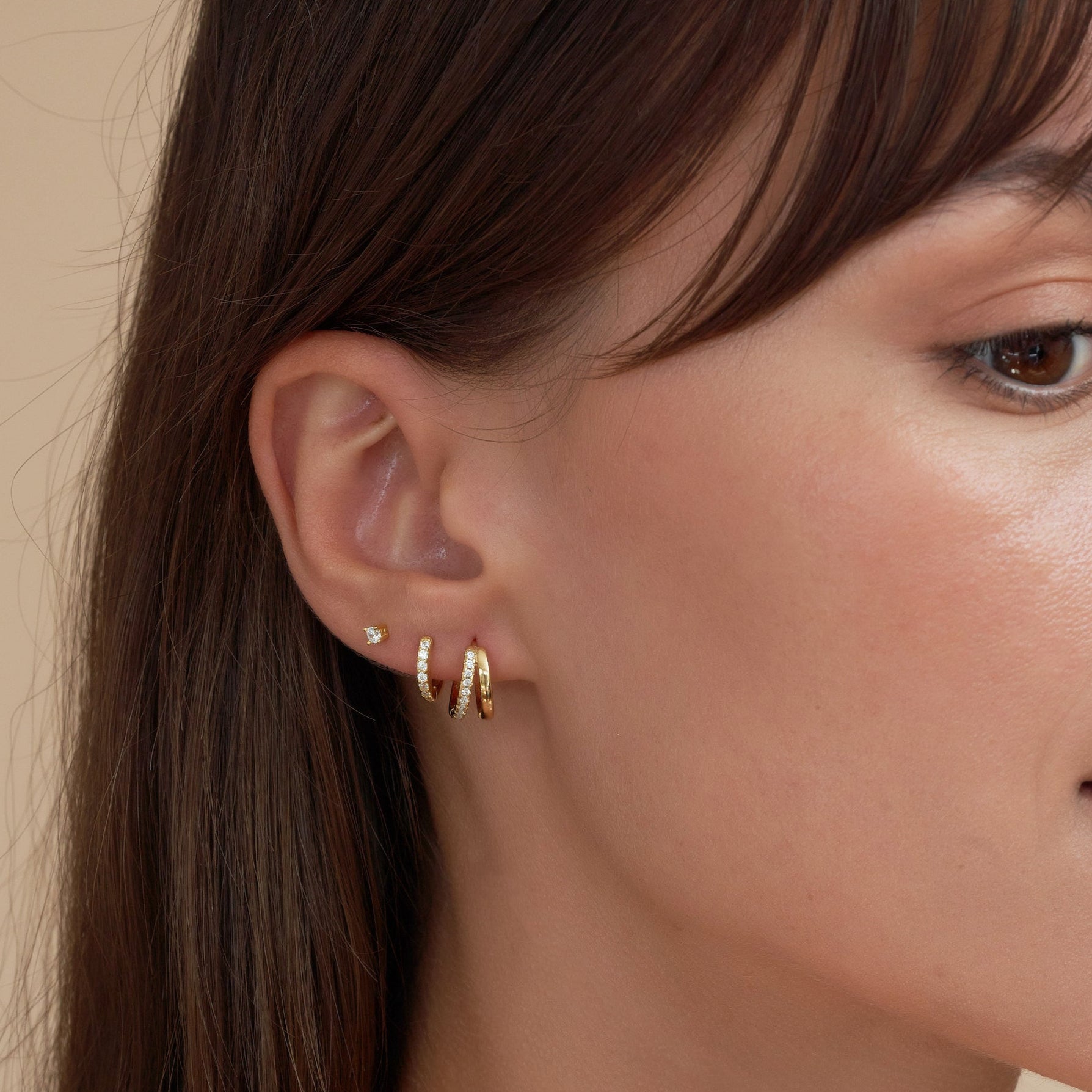 Close-up of a woman wearing gold hoop earrings with a neutral background