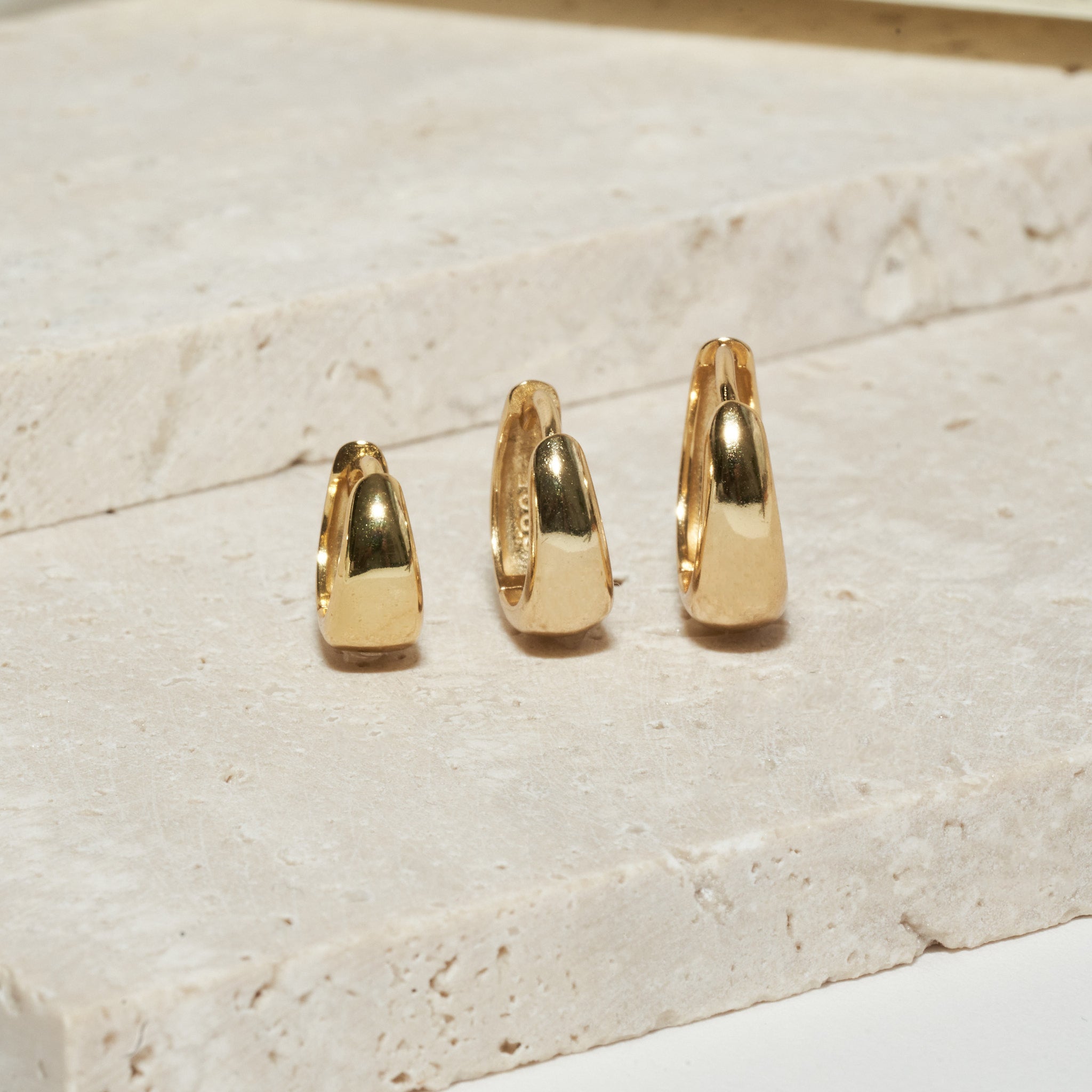 Three gold hoop earrings on a light stone surface