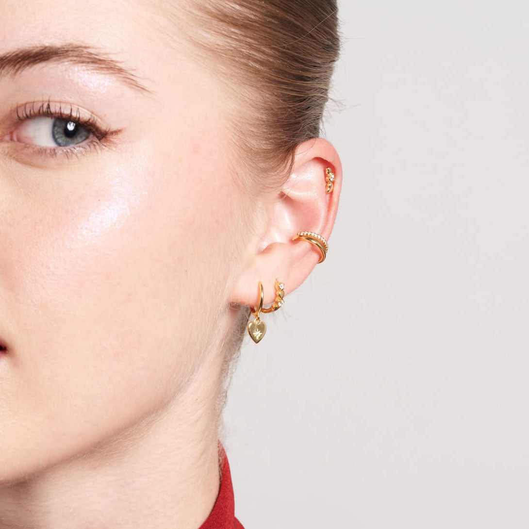 Close-up of a person's ear with gold earrings on a neutral background