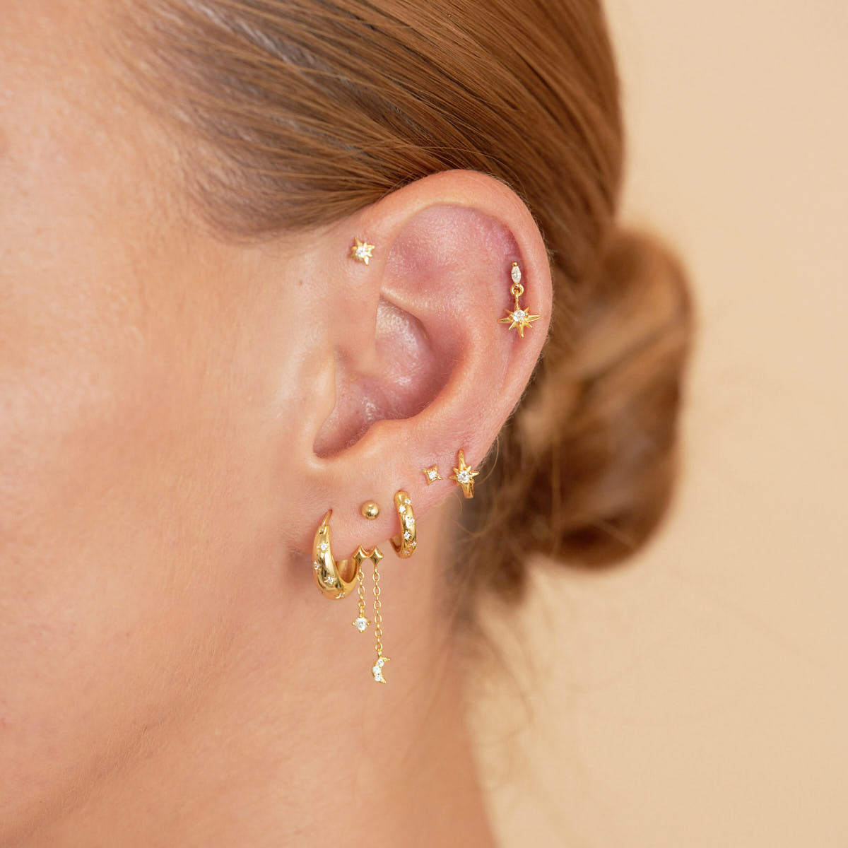 Close-up of an ear with gold earrings on a beige background