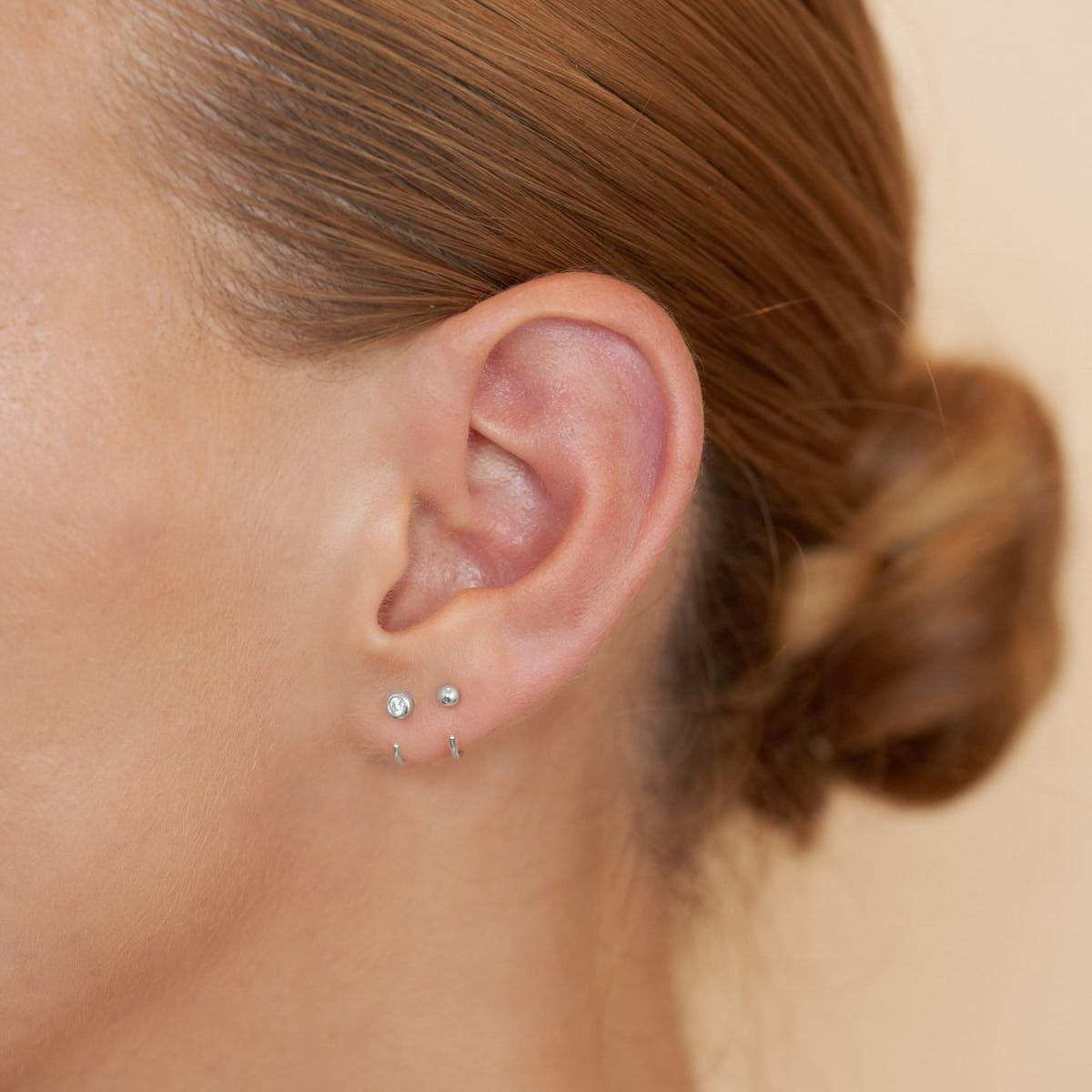 Close-up of an ear with two small earrings on a neutral background