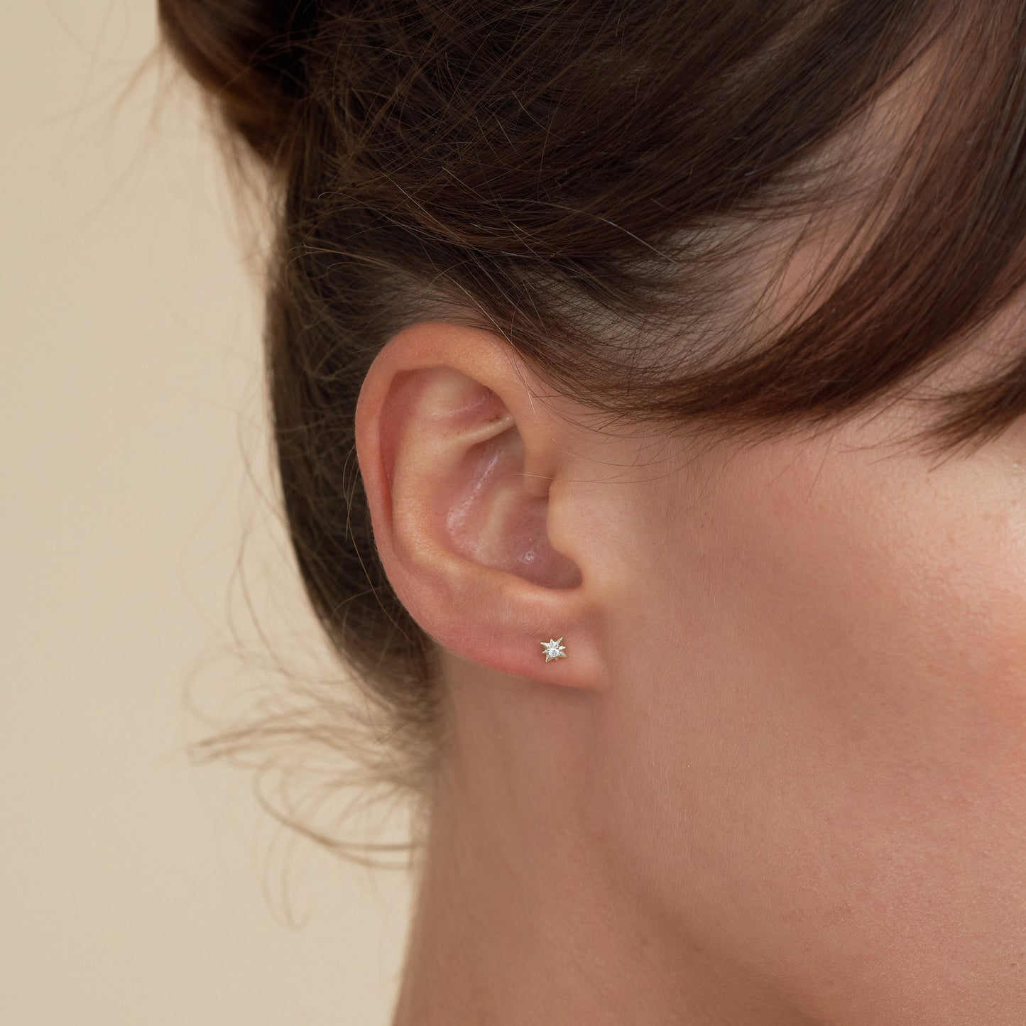 Close-up of an ear wearing a diamond stud earring on a beige background