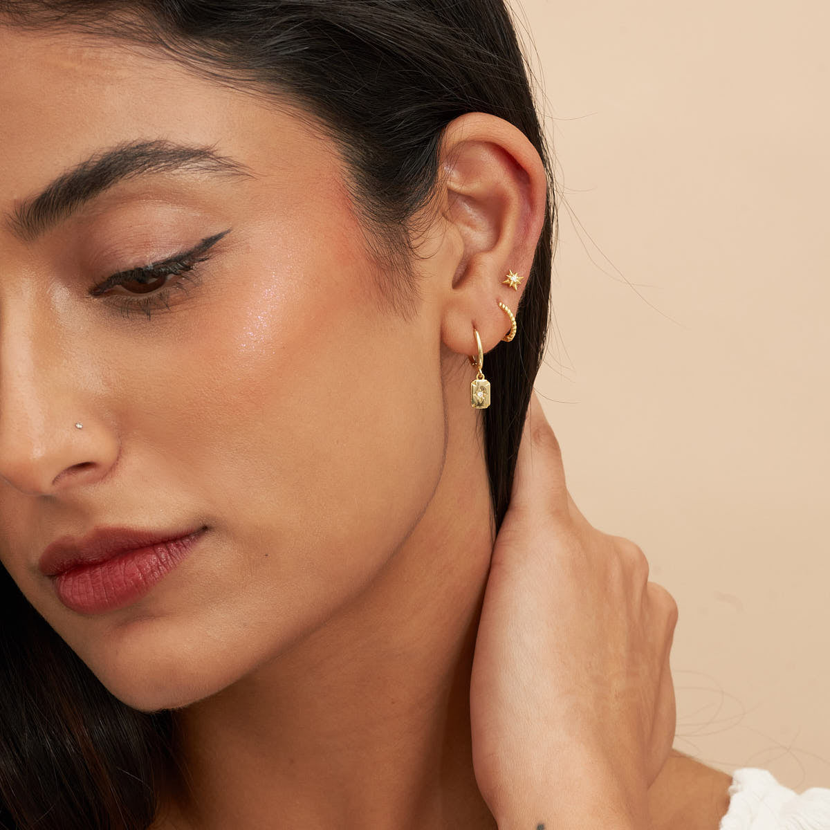 Close-up of a woman wearing gold hoop earrings with a beige background