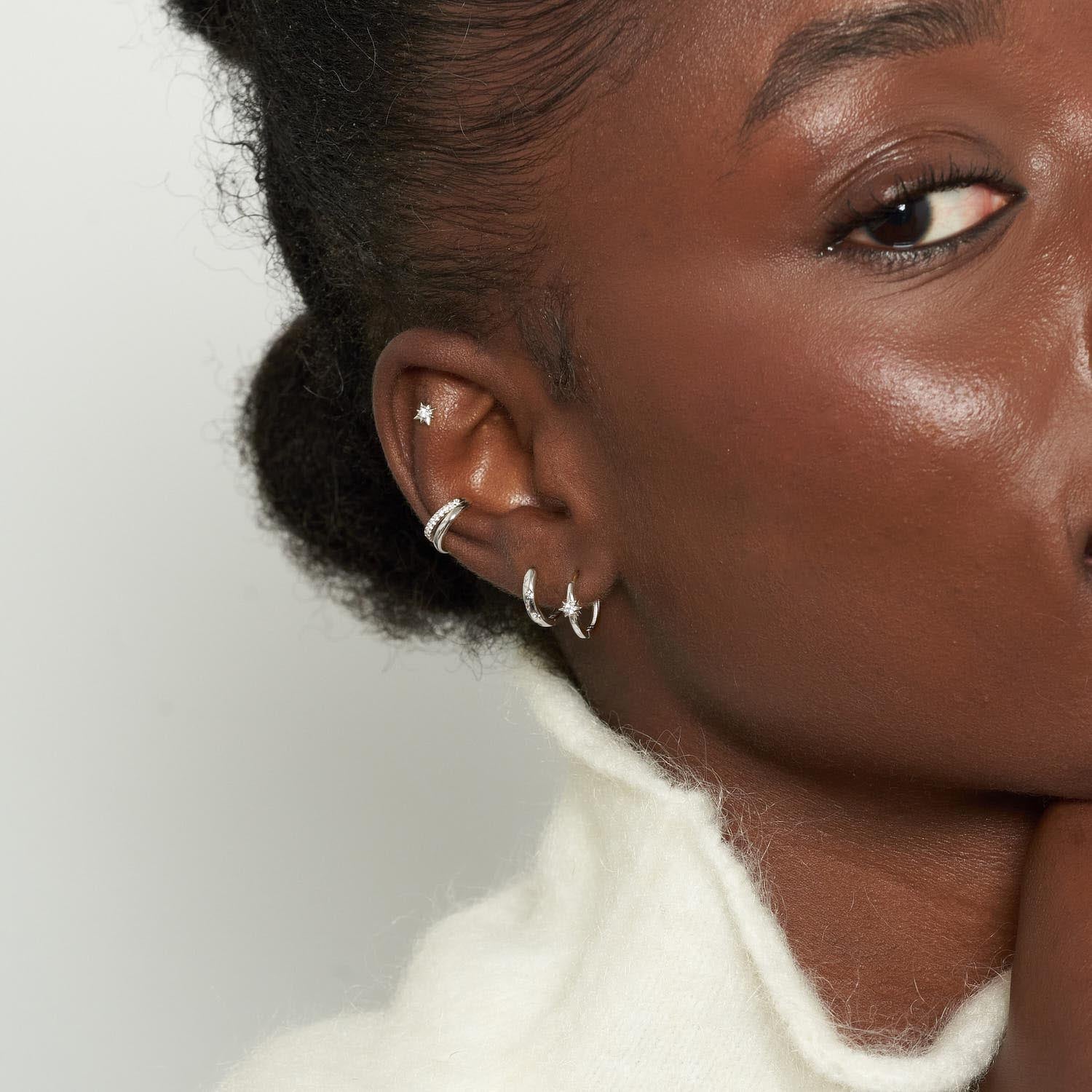 Close-up of a woman's ear with silver hoop earrings against a neutral background