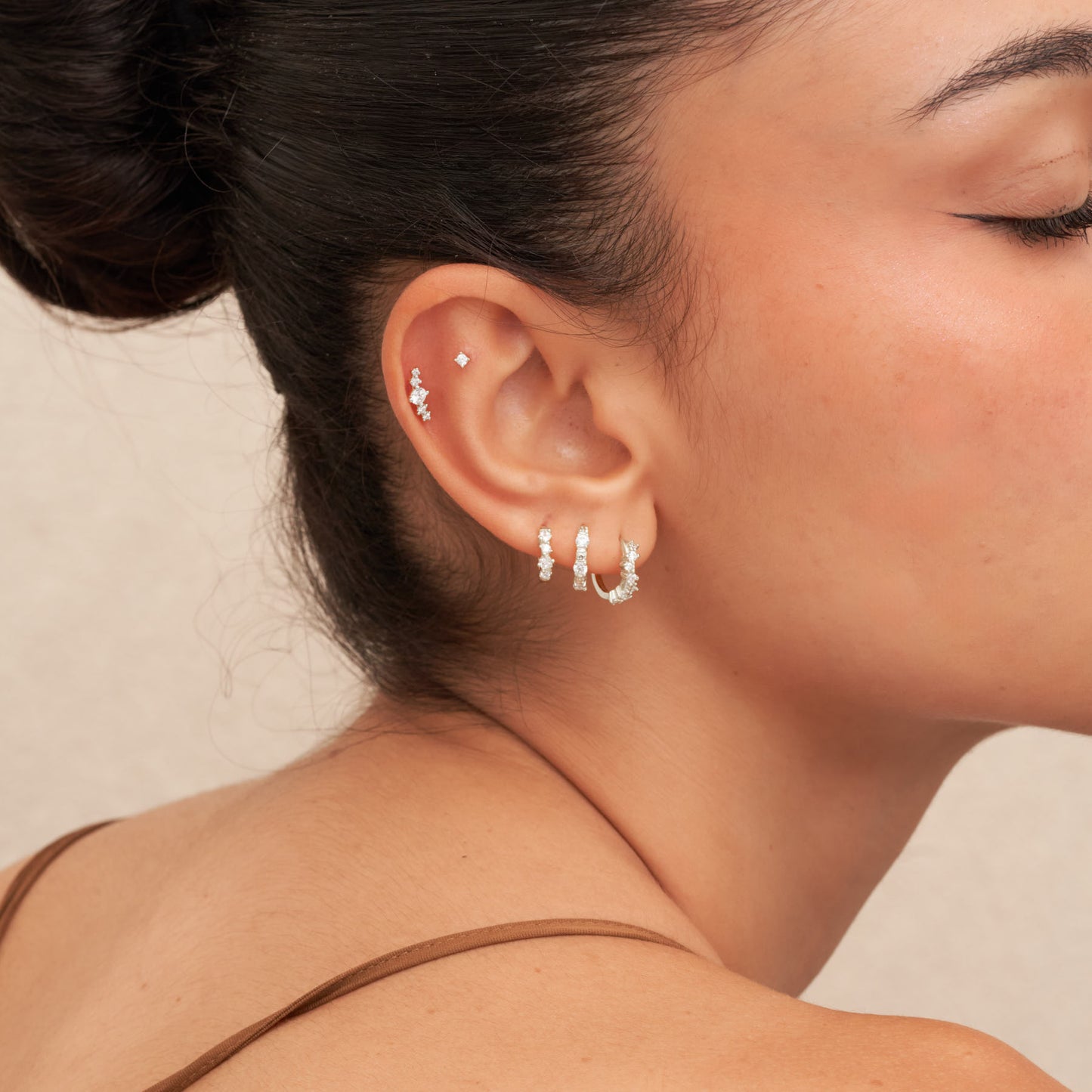 Close-up of a woman's ear wearing multiple earrings against a neutral background
