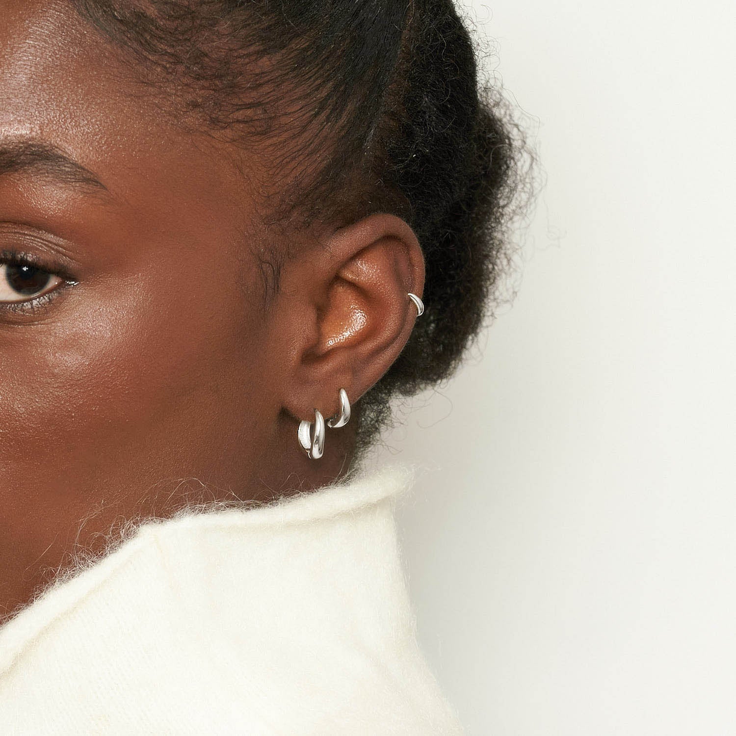 Close-up of a person wearing silver hoop earrings with a neutral background