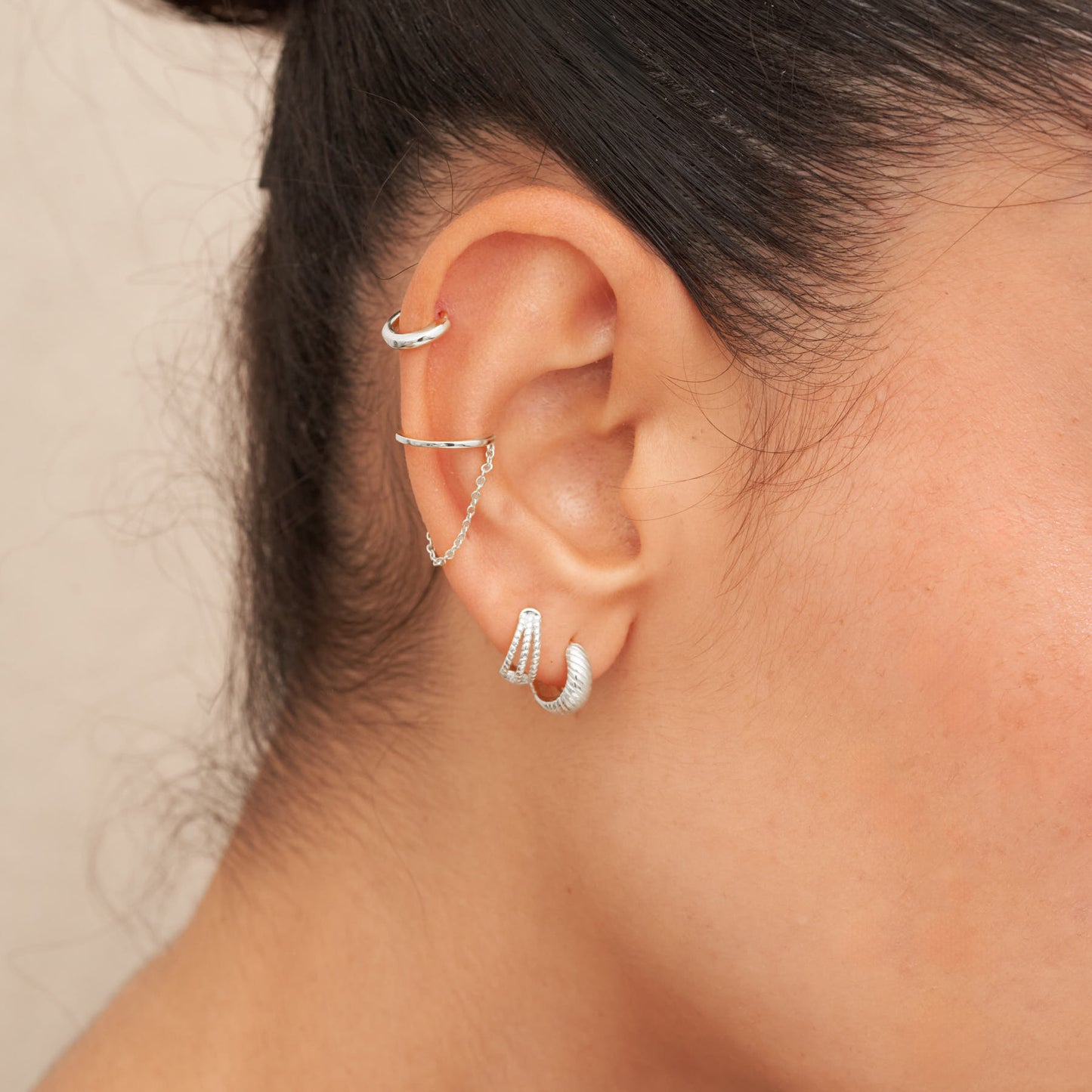 Close-up of an ear wearing multiple silver hoop earrings with a neutral background