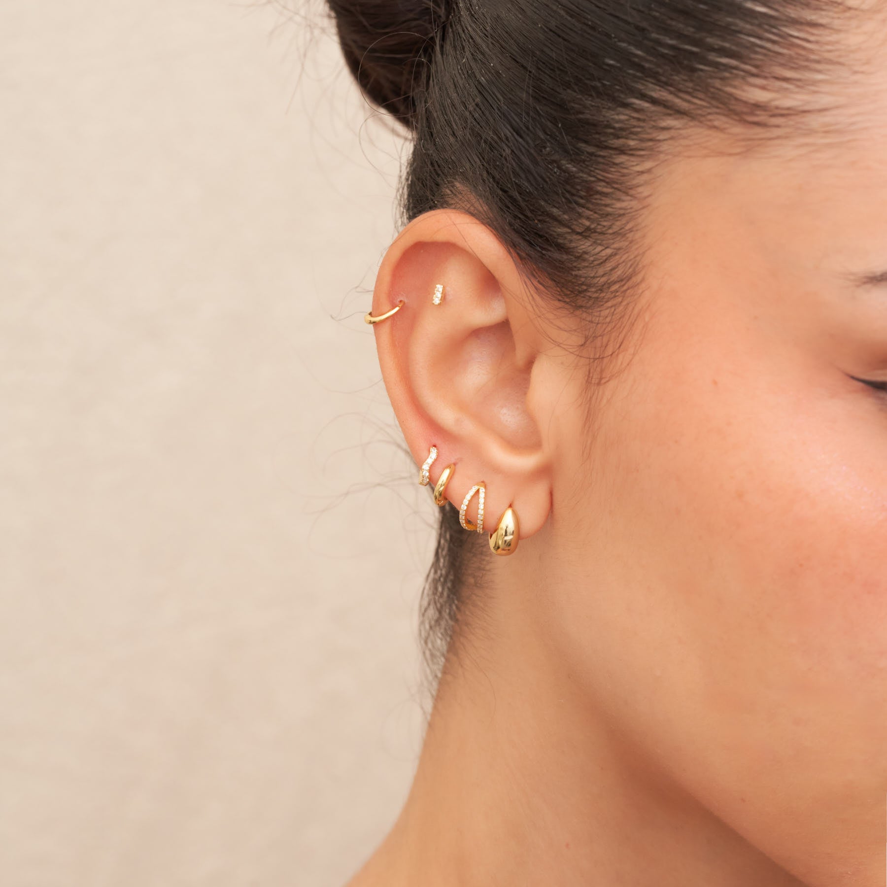 Close-up of an ear with gold earrings against a neutral background