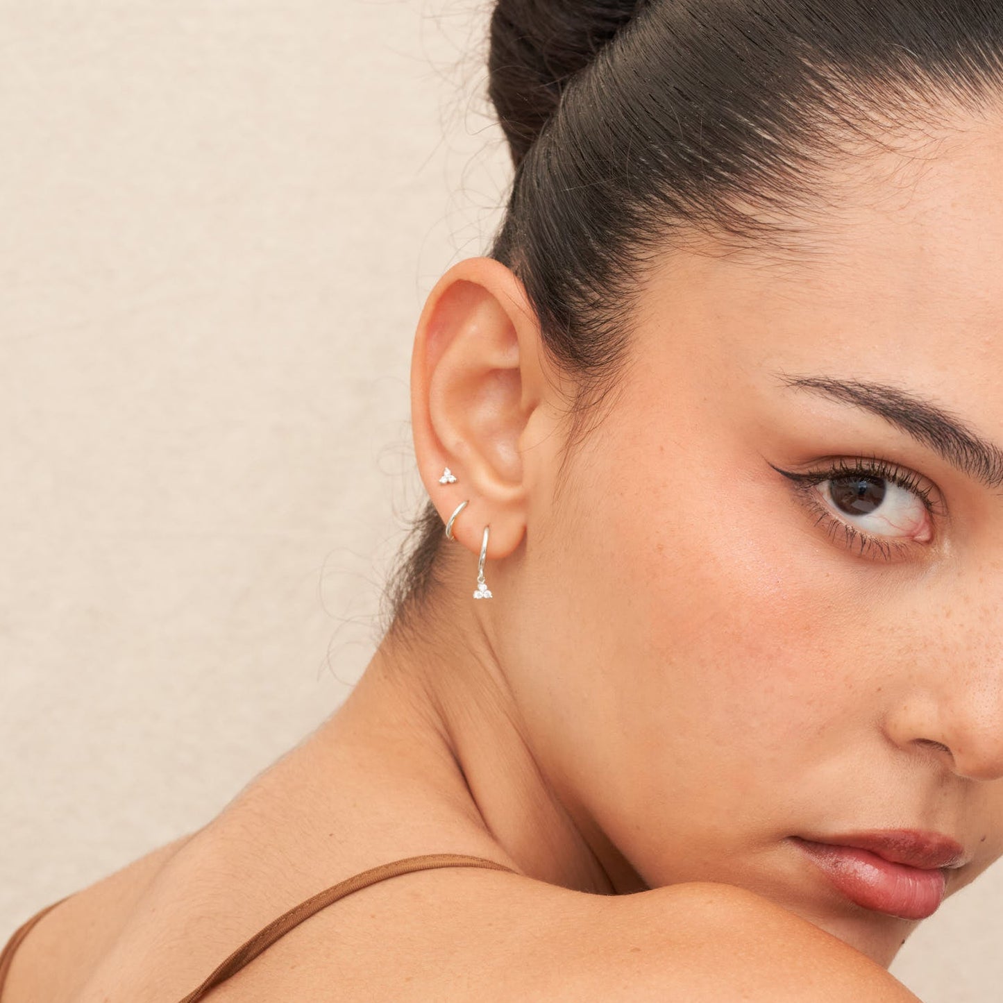 Close-up of a woman wearing a delicate earring against a neutral background