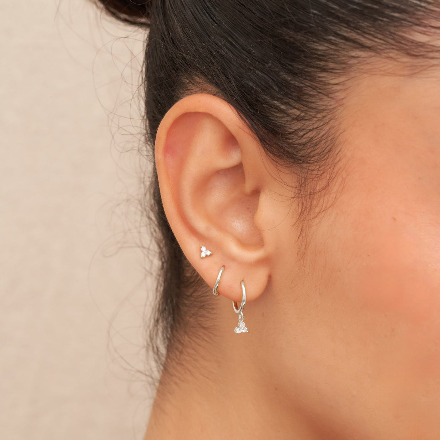 Close-up of a person wearing silver earrings against a neutral background