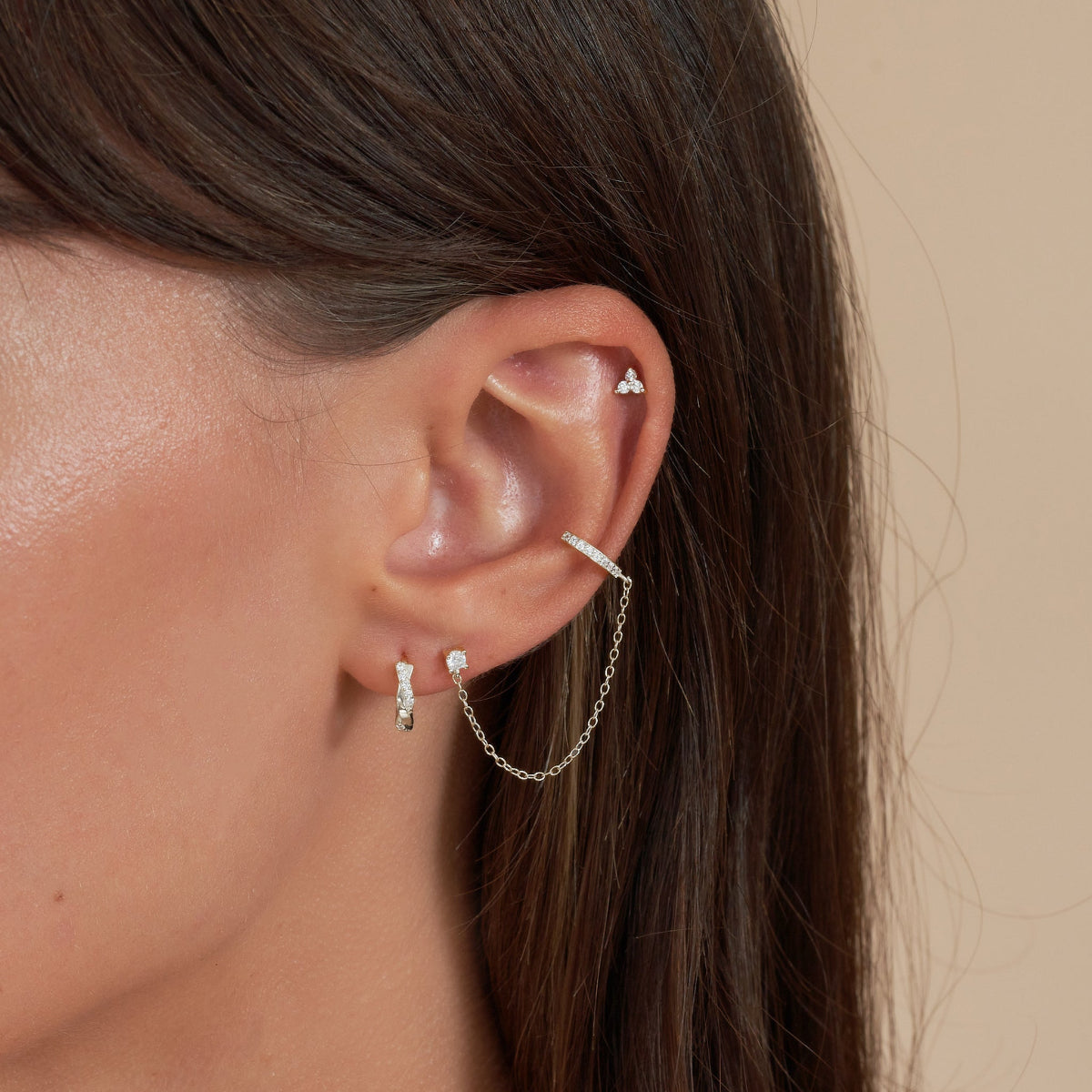 Close-up of an ear wearing multiple earrings with a neutral background
