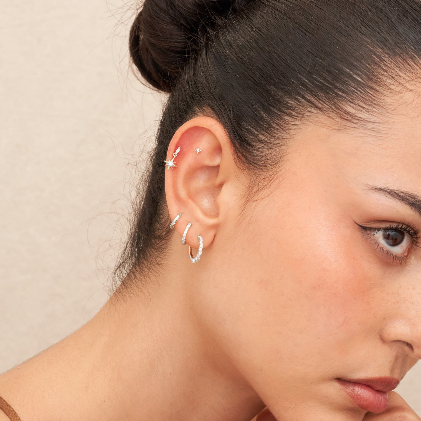 Close-up of a woman's ear wearing silver hoop earrings with a neutral background