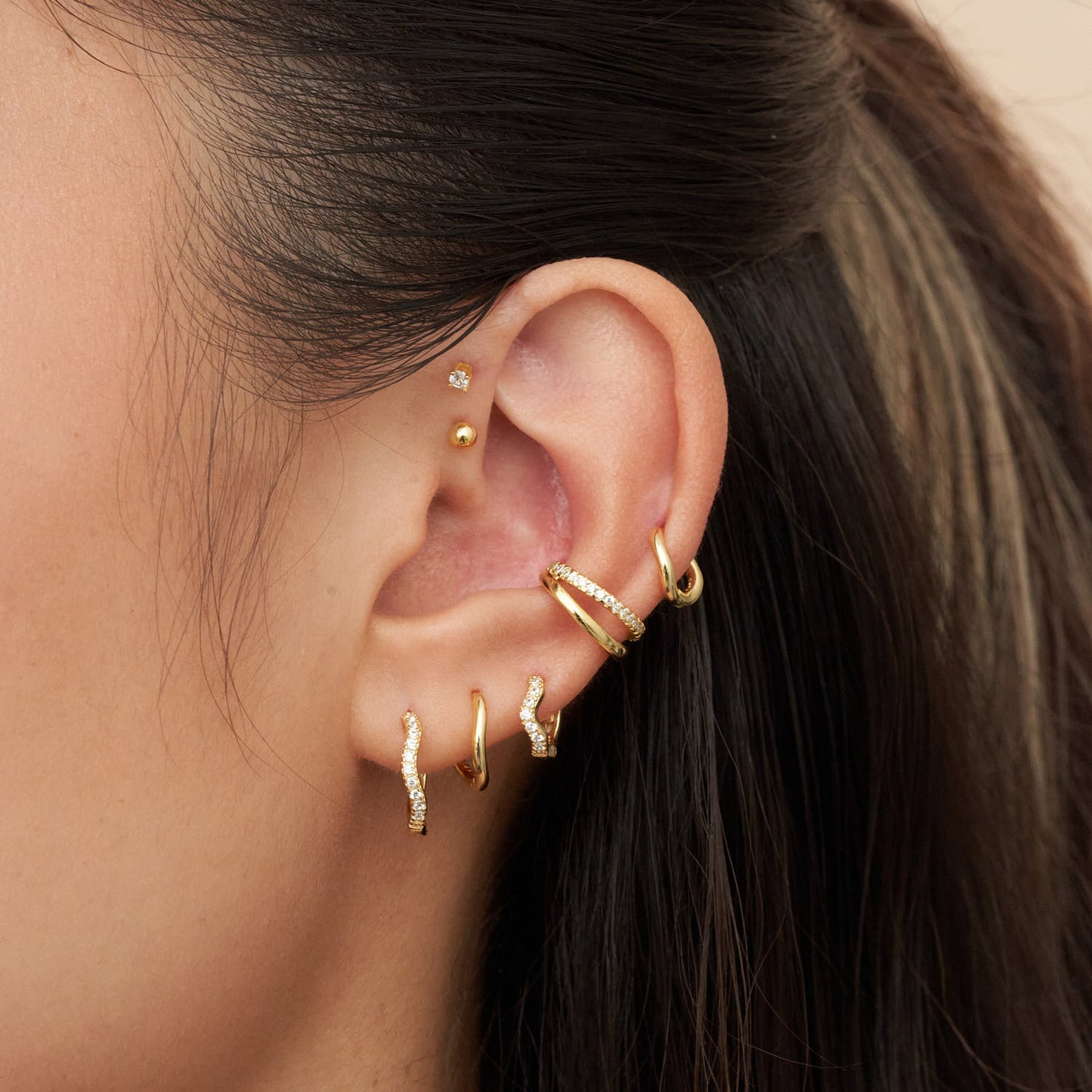 Close-up of an ear with multiple gold earrings against a neutral background