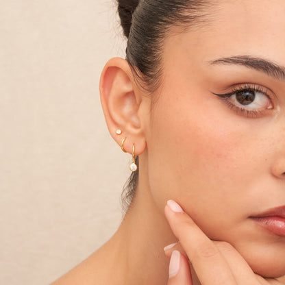 Close-up of a woman wearing gold earrings with a beige background