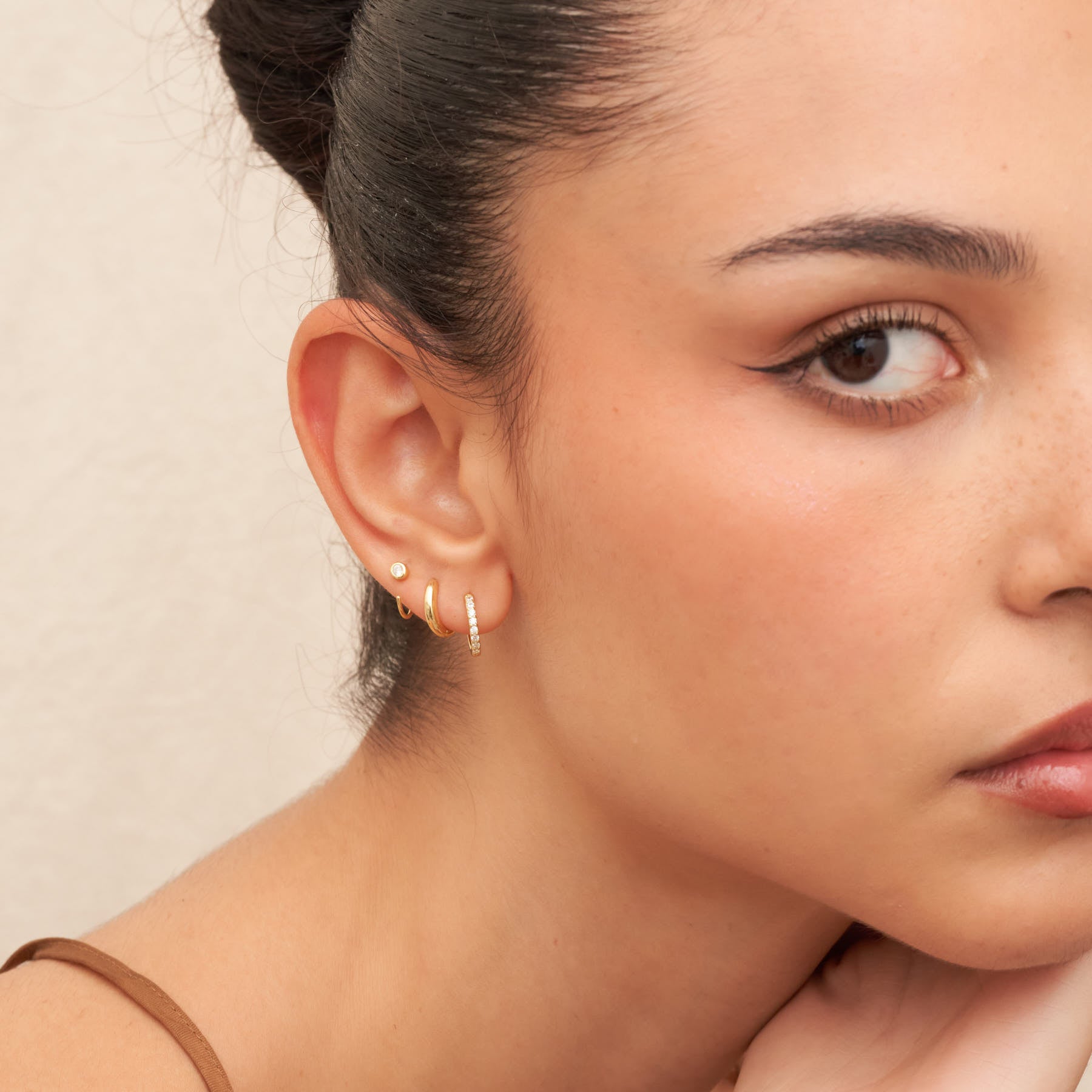 Close-up of a woman wearing gold hoop earrings against a neutral background
