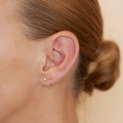 Close-up of an ear with gold earrings on a neutral background