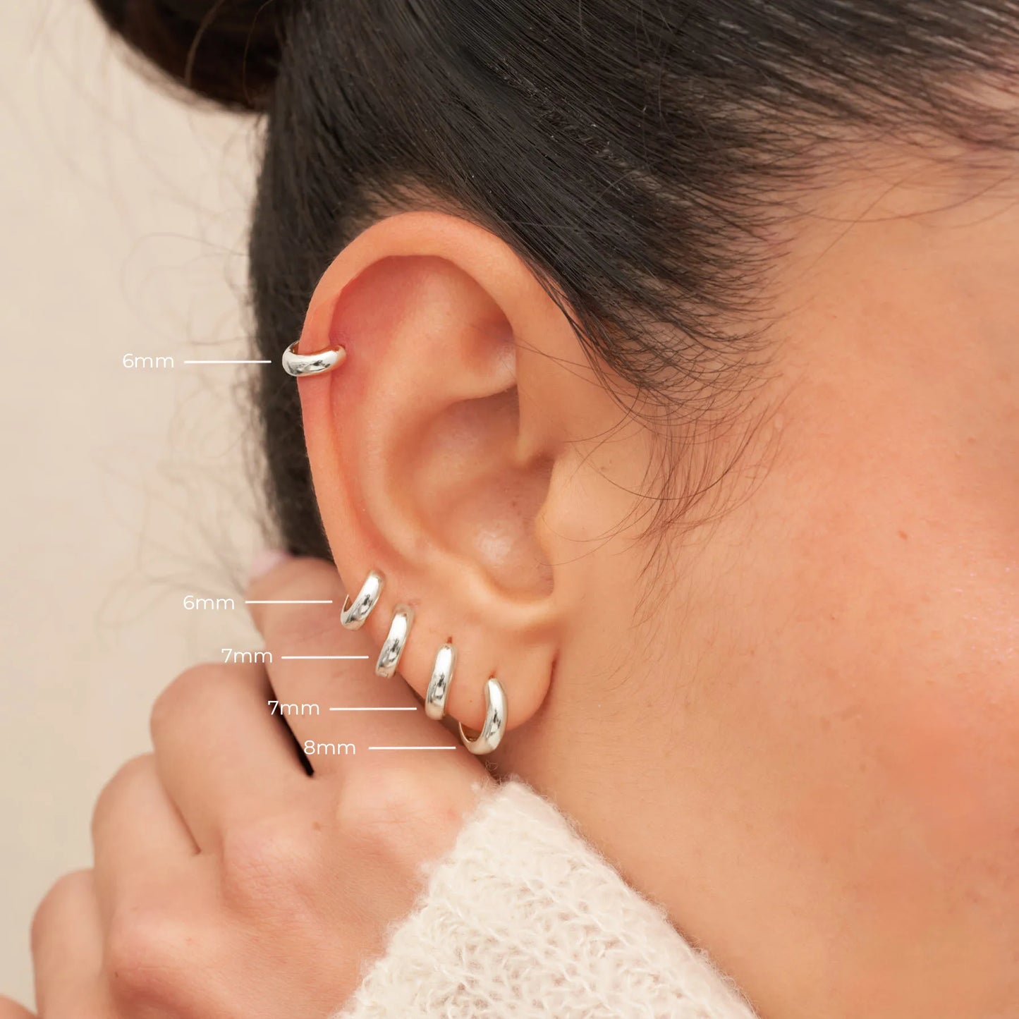 Close-up of an ear with silver hoop earrings labeled by size.