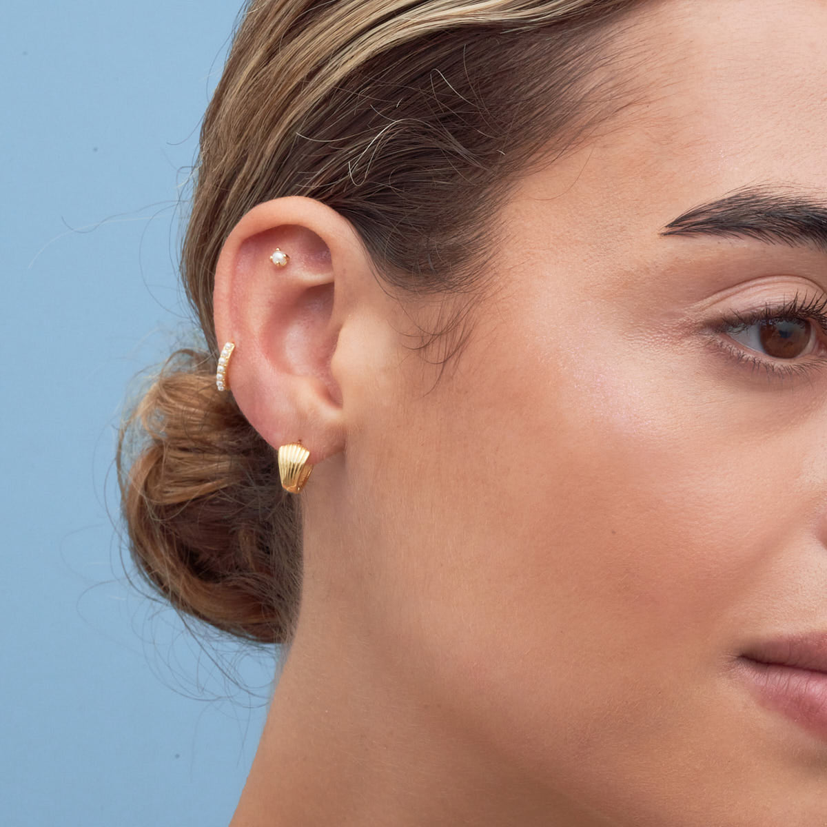Close-up of a woman's ear with gold earrings against a blue background