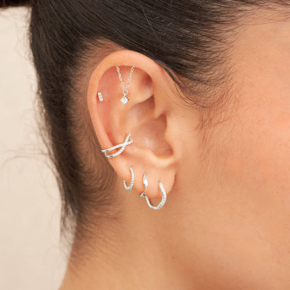 Close-up of an ear with multiple silver earrings on a neutral background