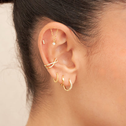 Close-up of an ear with gold earrings on a neutral background