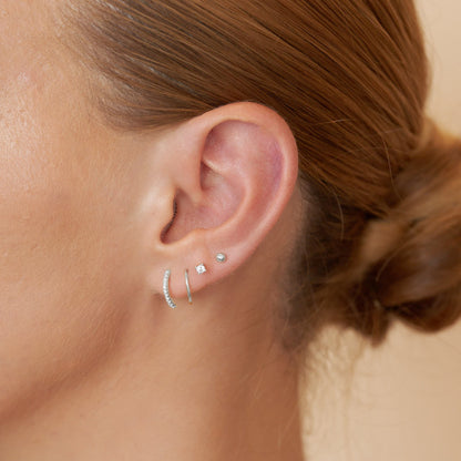 Close-up of an ear wearing multiple earrings with a neutral background