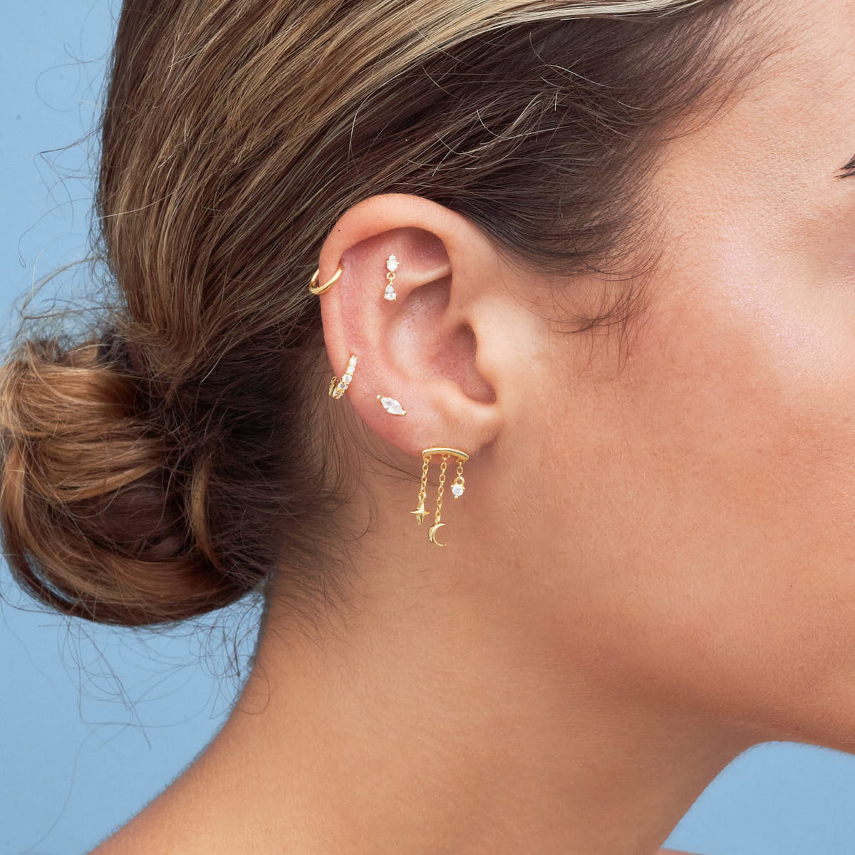 Close-up of an ear with gold earrings against a blue background