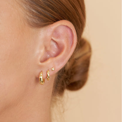 Close-up of an ear wearing gold hoop earrings with a neutral background