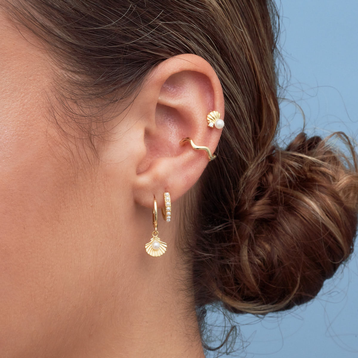 Close-up of an ear with gold earrings against a blue background