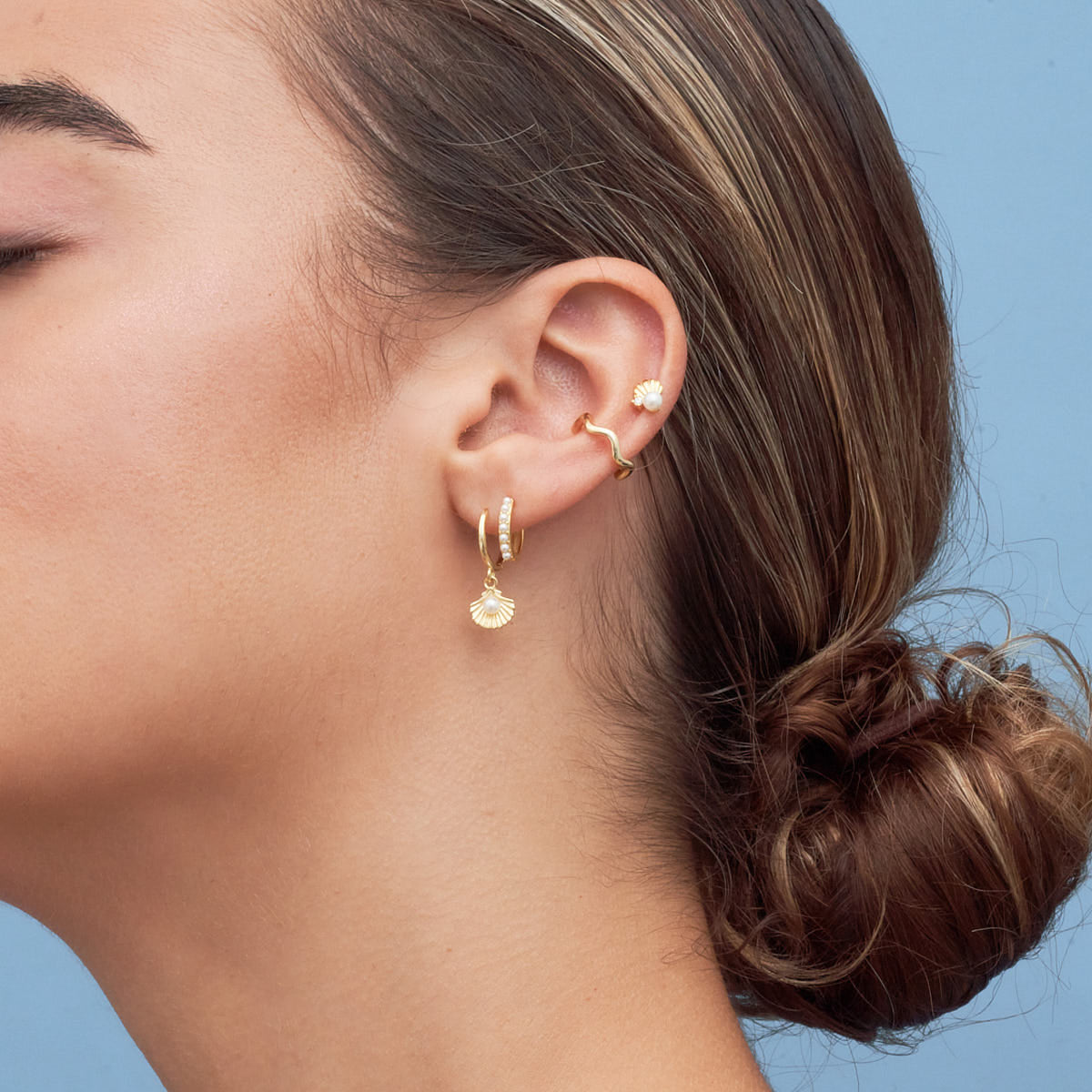Close-up of a person wearing gold hoop earrings against a blue background
