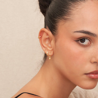Close-up of a woman's ear with gold hoop earrings against a neutral background