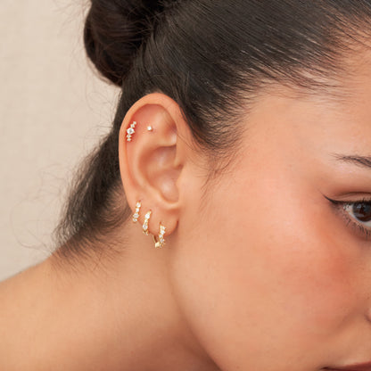 Close-up of a person wearing gold earrings with a neutral background