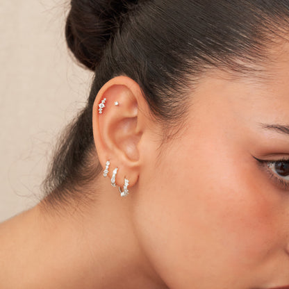 Close-up of a person's ear with multiple diamond earrings against a neutral background