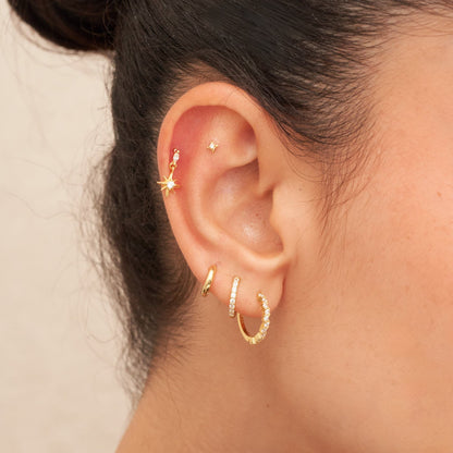 Close-up of an ear with gold earrings on a neutral background
