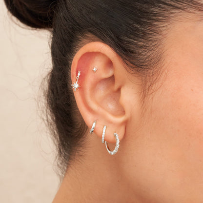 Close-up of an ear with multiple earrings on a neutral background