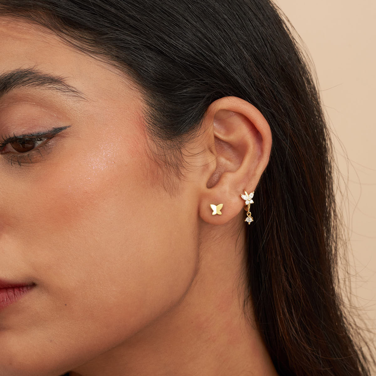 Close-up of a woman wearing gold butterfly earrings against a neutral background