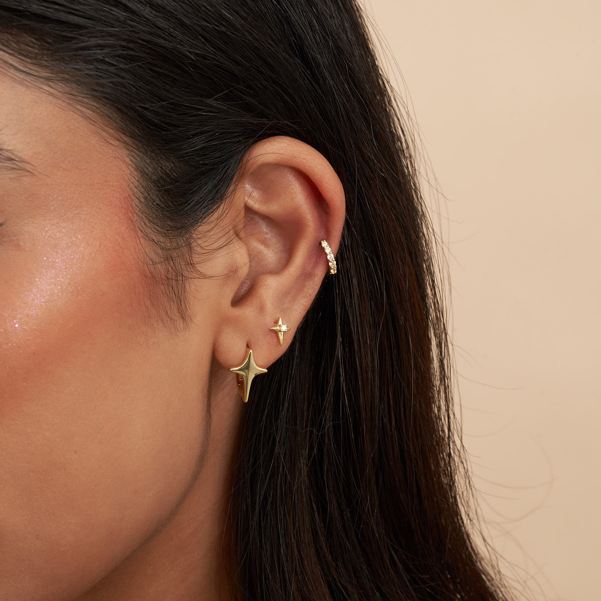 Close-up of a person wearing gold star-shaped earrings against a beige background