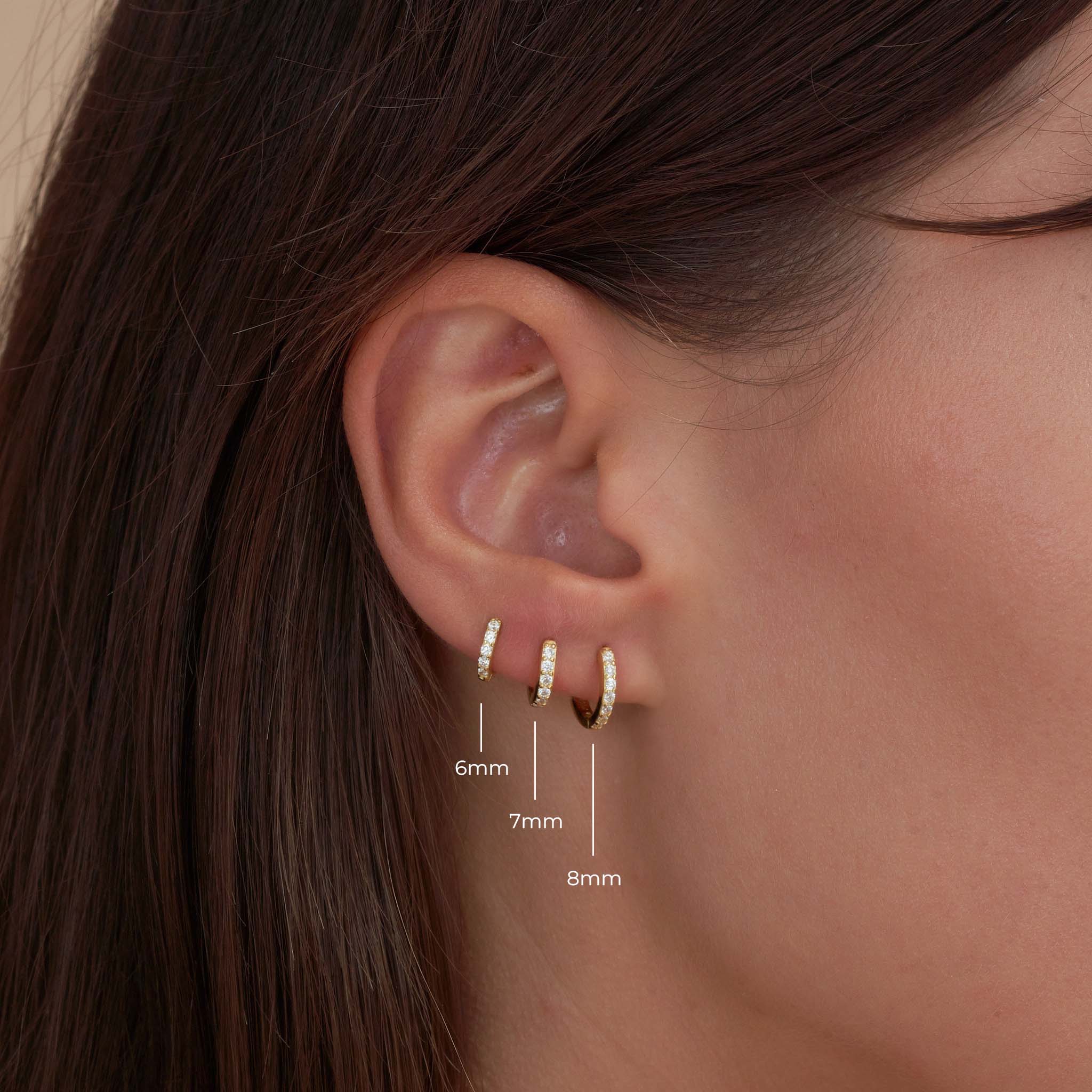 Close-up of an ear wearing gold hoop earrings with size measurements.