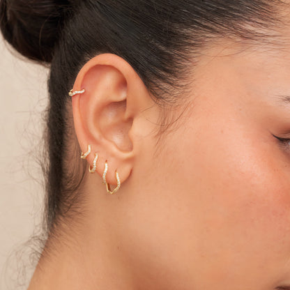 Close-up of a person wearing gold hoop earrings with a neutral background