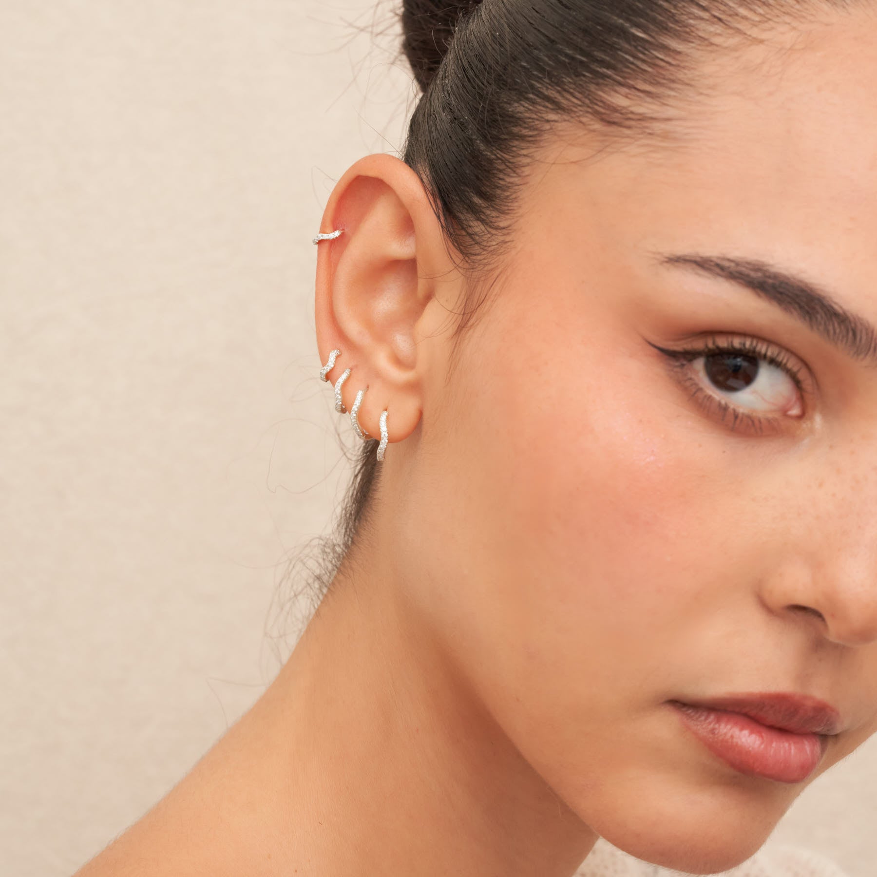 Close-up of a woman's ear with silver hoop earrings against a neutral background