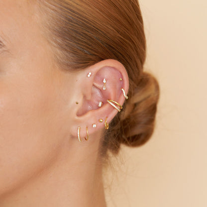 Close-up of an ear with multiple gold earrings on a beige background